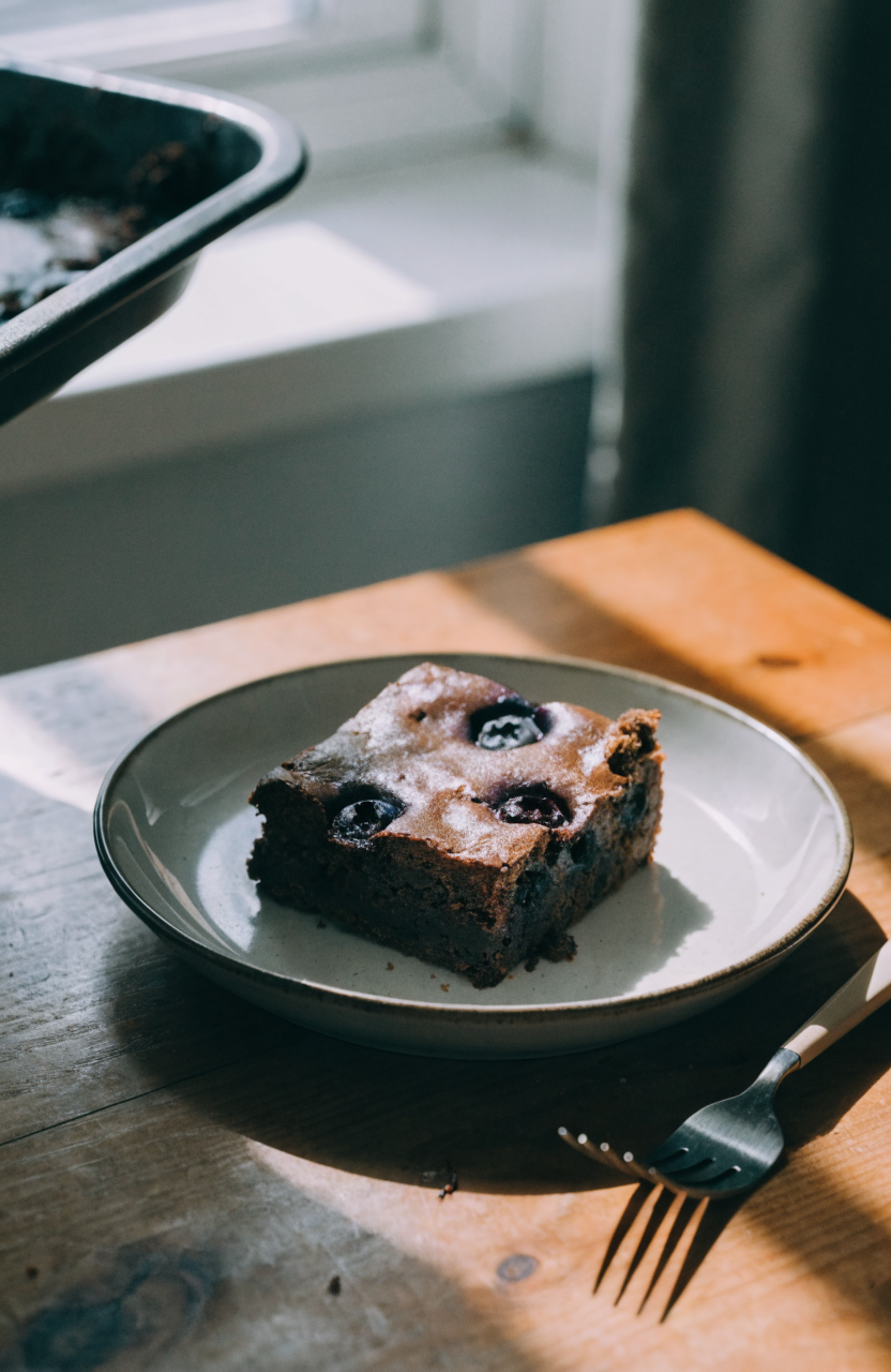 Square of blueberry brownies on a white plate showing blueberry pockets and fudgy crumb